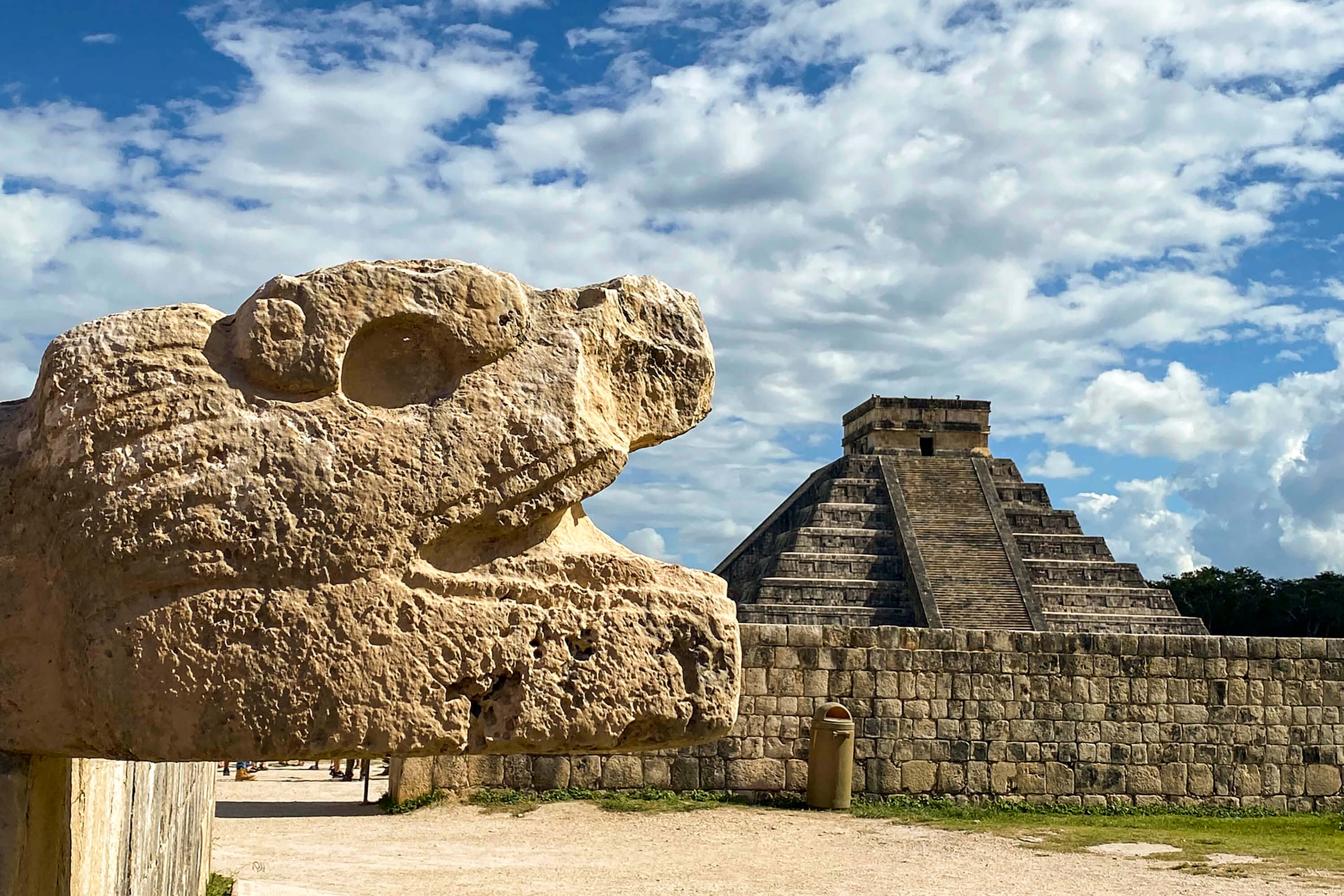 Cabeza de serpiente esculpida en Chichén Itzá con la Pirámide de Kukulcán al fondo