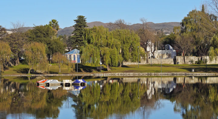 Parque con lago rodeado de arboles y montaña al fondo, Alta Gracia, Córdoba