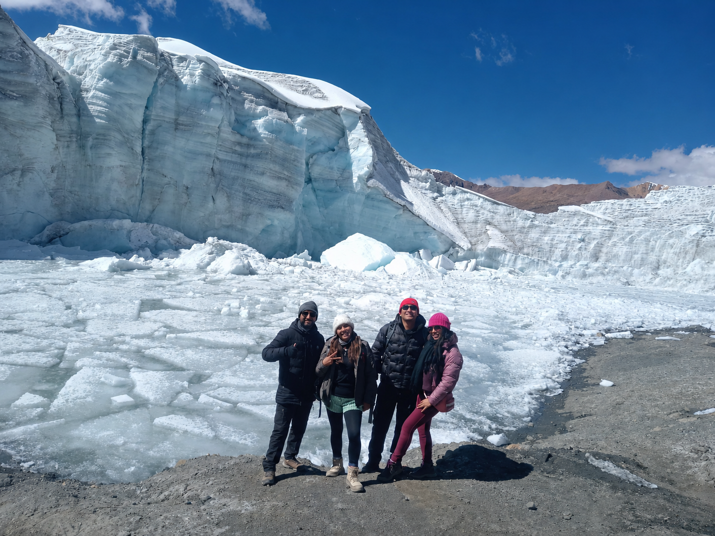Grupo de cuatro viajeros posando frente al frente del Glaciar Quelccaya con bloques de hielo alrededor