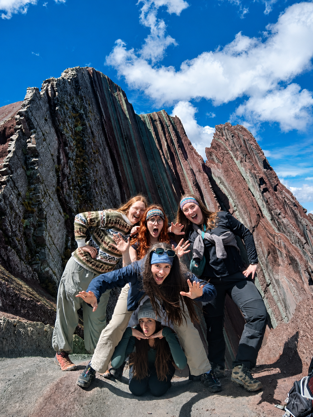 Grupo de viajeras posa con entusiasmo frente a formaciones rocosas estratificadas de Pallay Punchu en Cusco