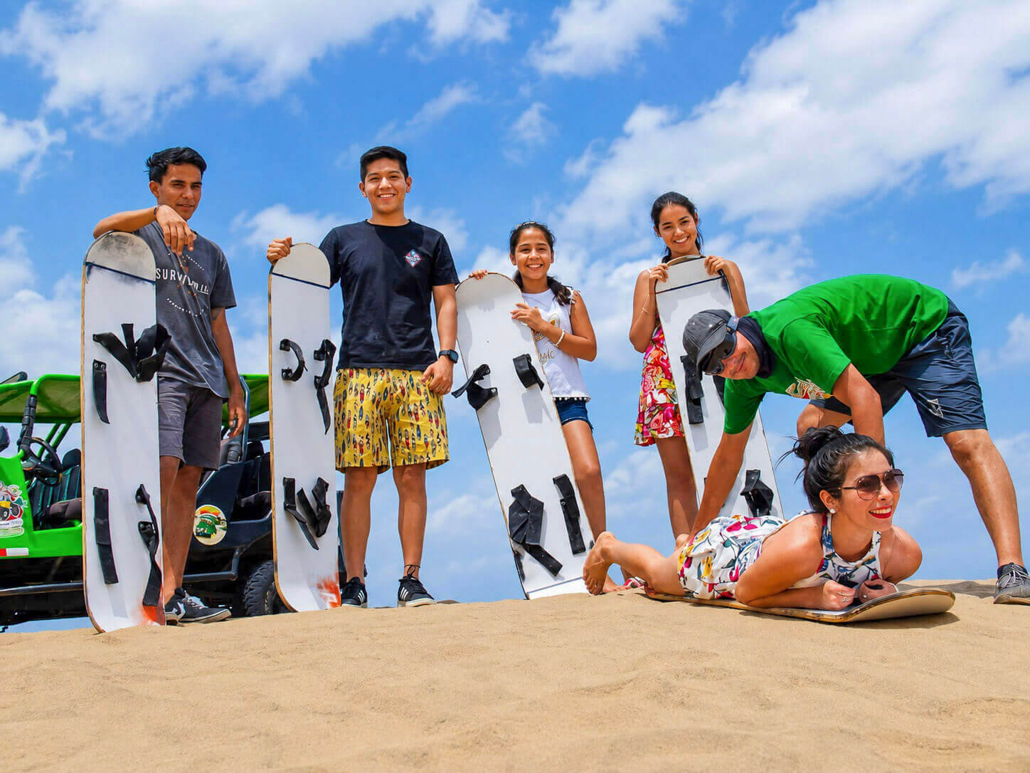 Guía preparando a una viajera para bajar en sandboard tendida sobre la tabla en una duna de Huacachina