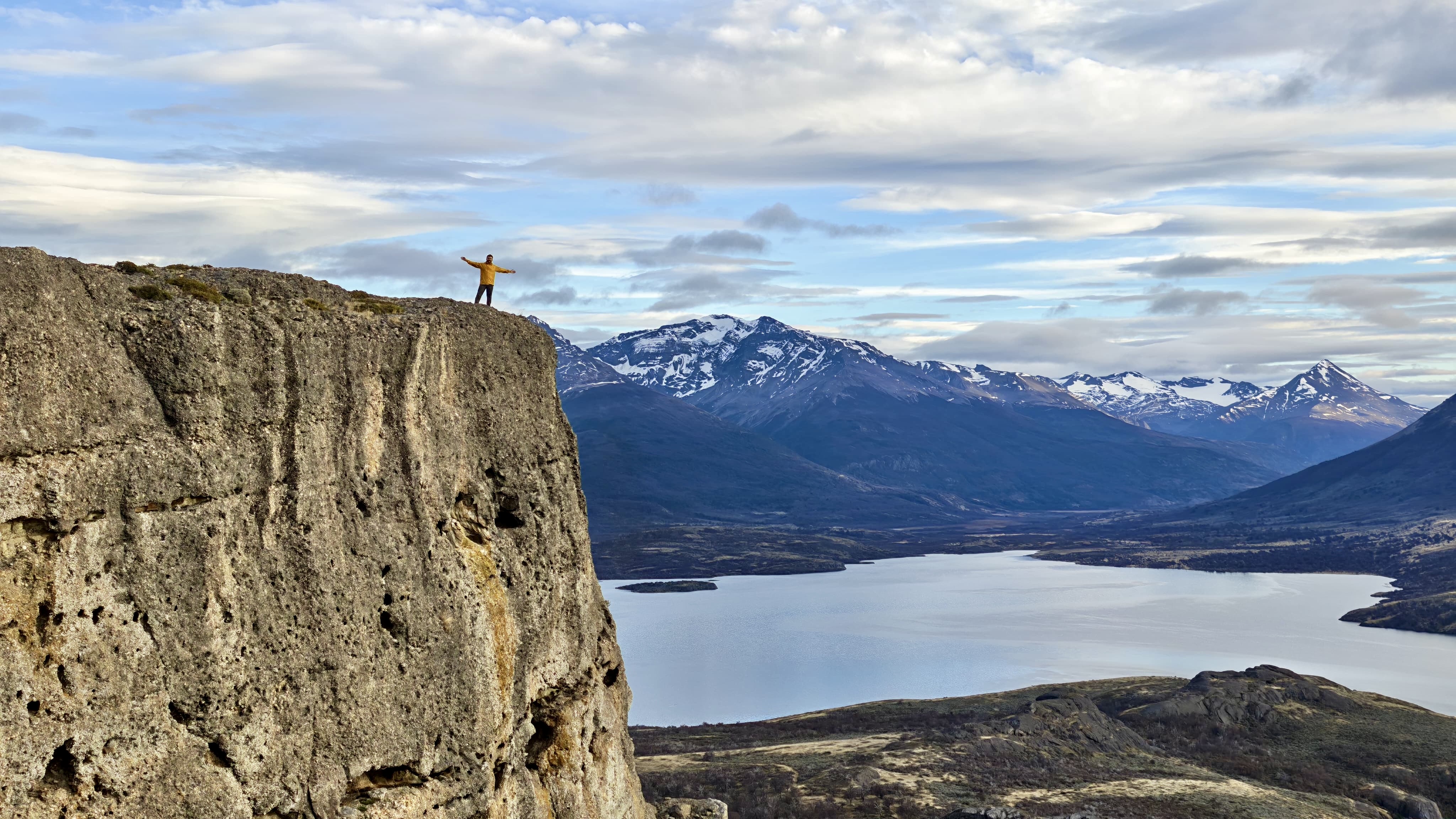 Turista con chaqueta amarilla en la cima del Cerro Benítez, con vista panorámica al lago y montañas
