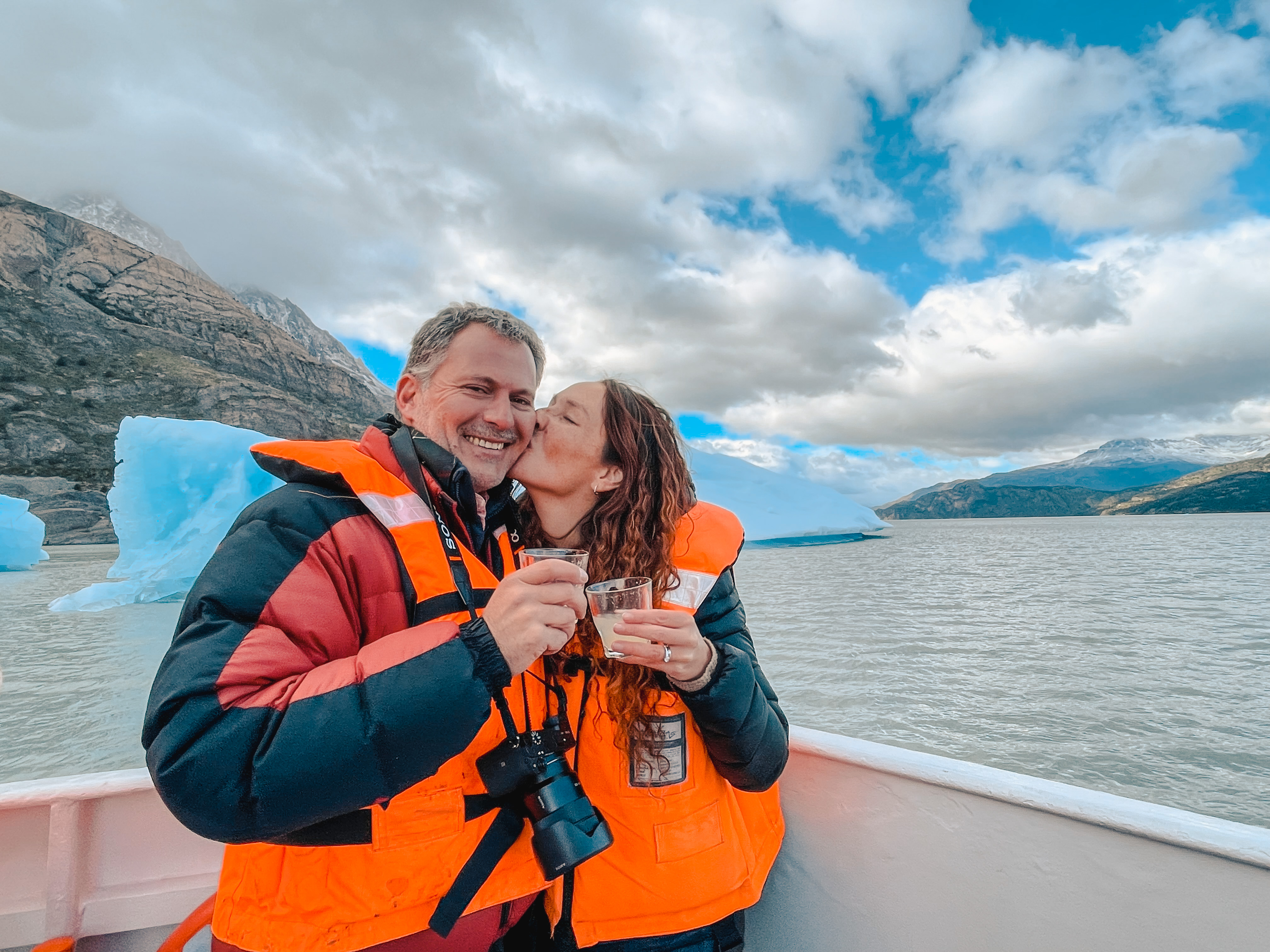 Pareja brindando en barco de navegación por Lago Grey con icebergs y montañas de fondo