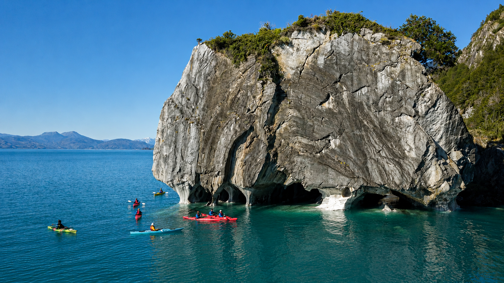Grupo de kayaks navegando hacia la Catedral de Mármol en Lago General Carrera con montañas de fondo