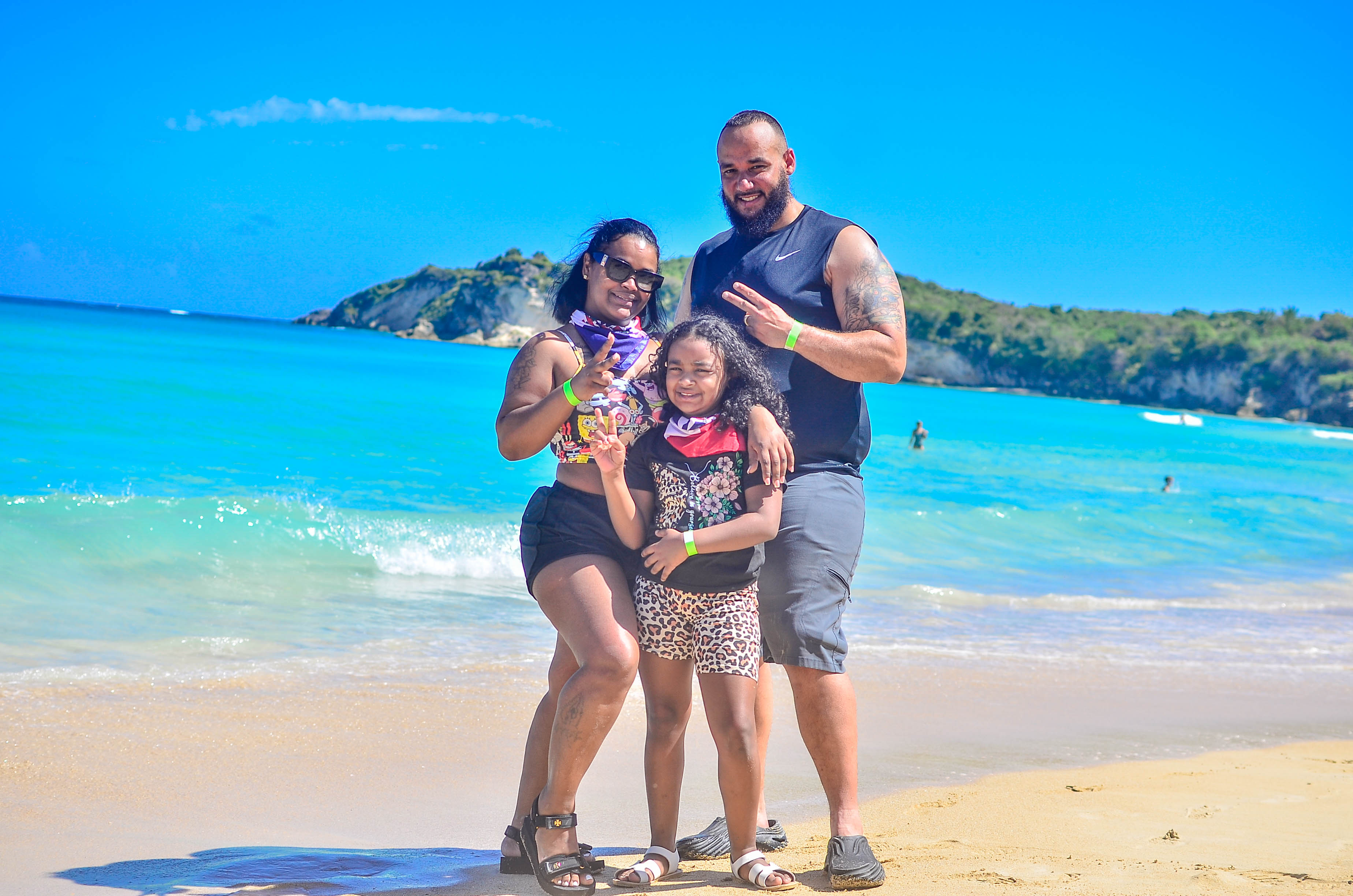 Familia con una niña posa en la arena de Playa Macao, con mar turquesa y promontorio verde al fondo