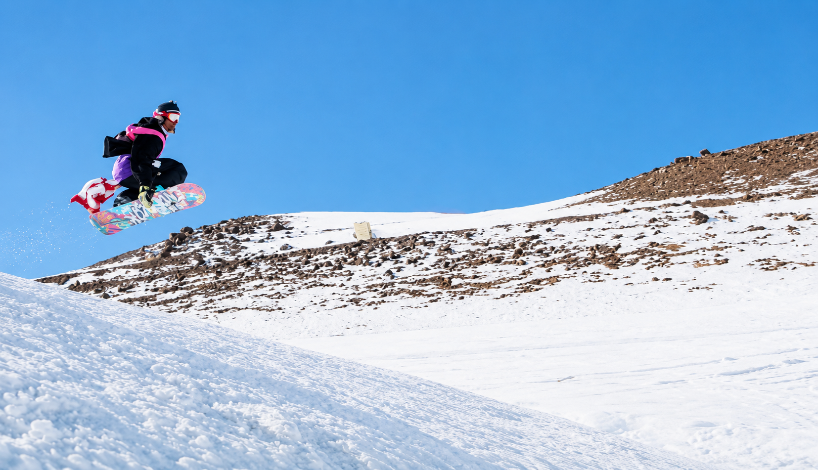Snowboarder saltando sobre terreno rocoso y nevado en las pistas de El Colorado