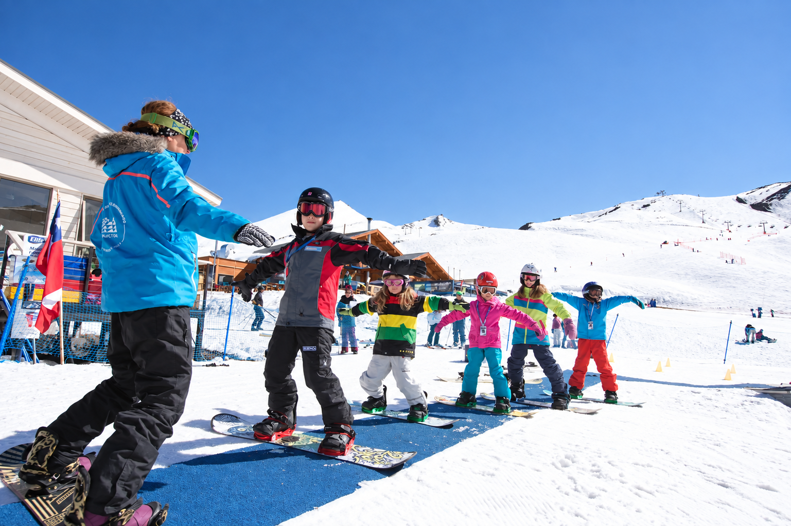 Instructora enseñando snowboard a grupo de niños en zona de principiantes de Valle Nevado